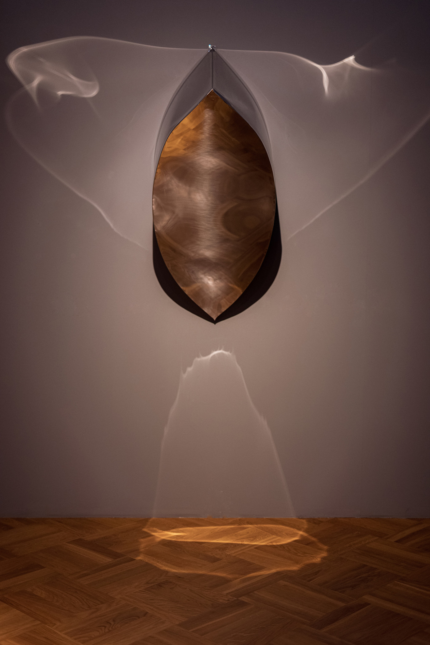the sculpture made of steel hanging on the wall and making reflections on the floor